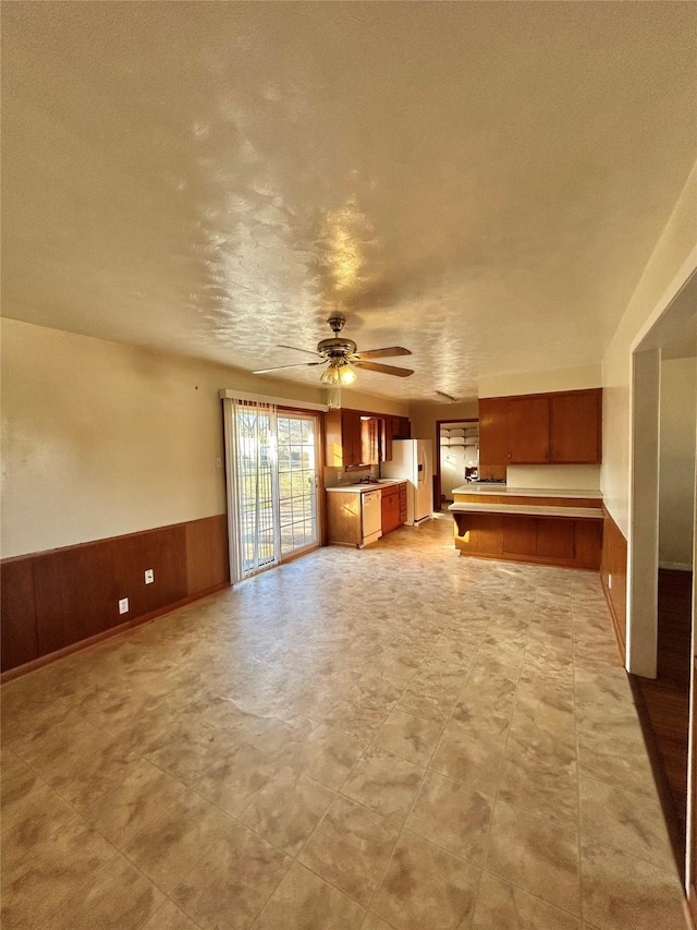 unfurnished living room with ceiling fan and wood walls