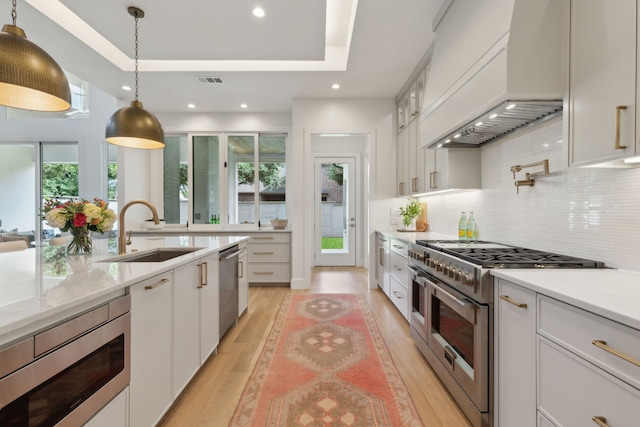 kitchen featuring premium range hood, sink, white cabinetry, appliances with stainless steel finishes, and a tray ceiling