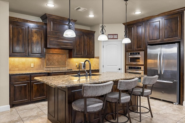 kitchen with stainless steel appliances, a kitchen island with sink, sink, and dark brown cabinetry