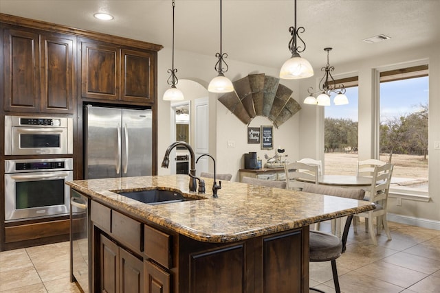 kitchen featuring stainless steel appliances, an island with sink, hanging light fixtures, and sink