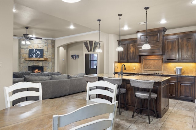 kitchen featuring a breakfast bar, pendant lighting, an island with sink, sink, and dark brown cabinetry