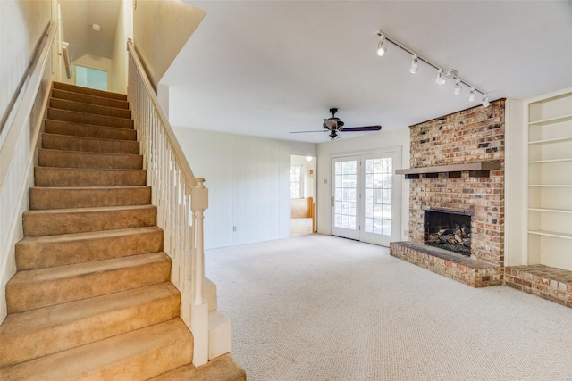 staircase with built in features, carpet floors, ceiling fan, a brick fireplace, and french doors