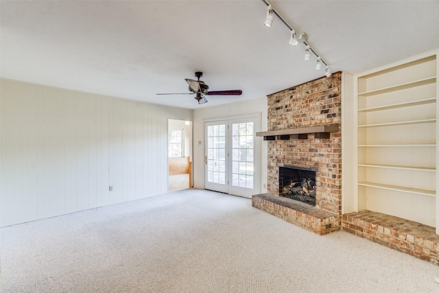 unfurnished living room with ceiling fan, carpet, a fireplace, track lighting, and built in shelves