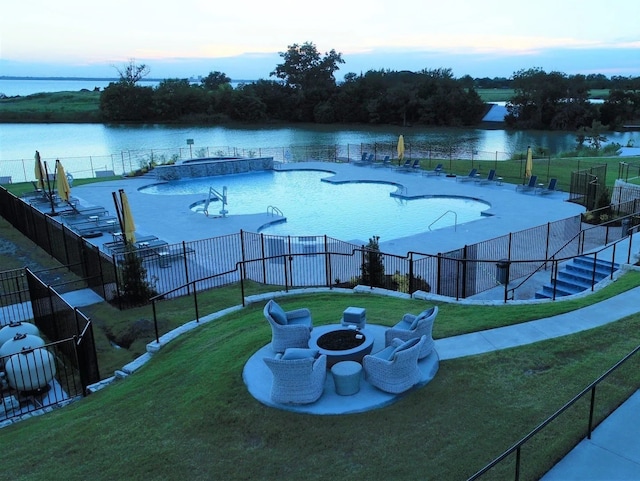 pool at dusk with a fire pit, a lawn, and a water view