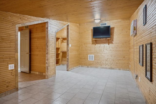 tiled spare room with wooden ceiling, visible vents, and wood walls