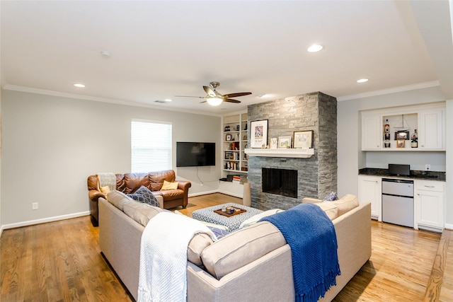 living room with ornamental molding, built in shelves, a fireplace, and light hardwood / wood-style floors