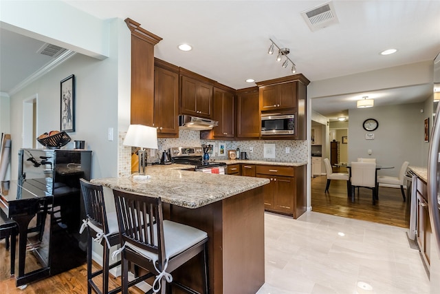 kitchen with tasteful backsplash, appliances with stainless steel finishes, kitchen peninsula, and light stone countertops