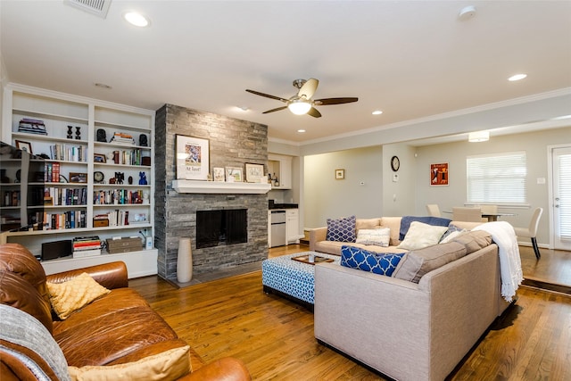 living room with ceiling fan, ornamental molding, wood-type flooring, and a stone fireplace