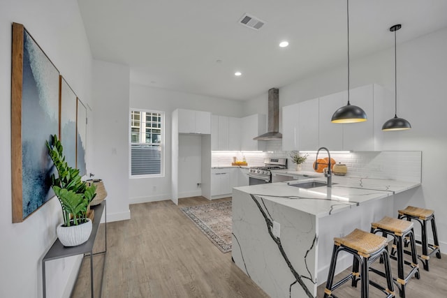 kitchen featuring wall chimney exhaust hood, sink, gas range, decorative light fixtures, and white cabinets