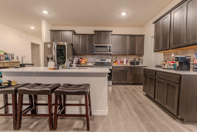 kitchen with appliances with stainless steel finishes, dark brown cabinets, a center island with sink, and a breakfast bar