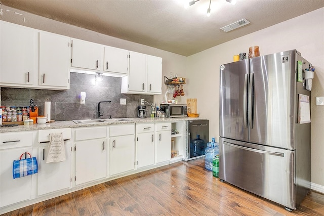 kitchen featuring sink, white cabinetry, appliances with stainless steel finishes, light hardwood / wood-style floors, and decorative backsplash