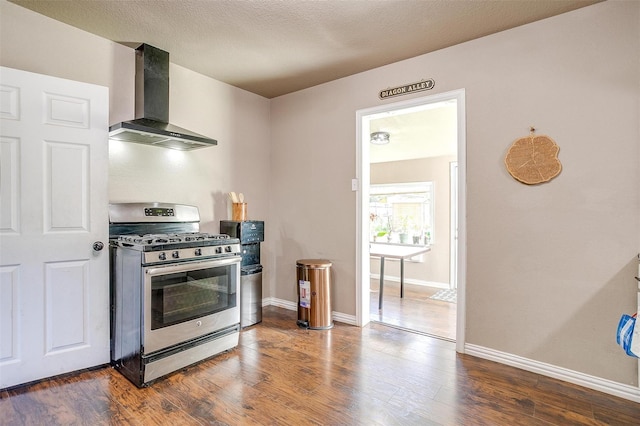 kitchen featuring dark wood-type flooring, wall chimney range hood, a textured ceiling, and stainless steel gas stove