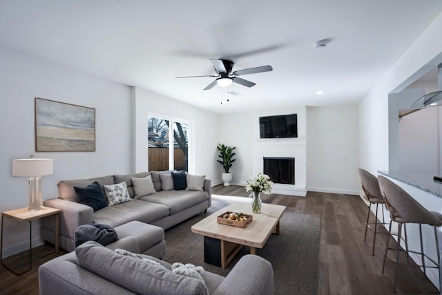 living room with ceiling fan, dark hardwood / wood-style floors, and a brick fireplace