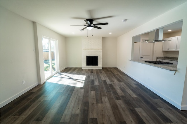 unfurnished living room featuring dark hardwood / wood-style flooring, a brick fireplace, and ceiling fan