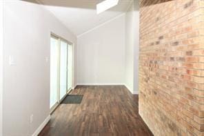 hallway featuring vaulted ceiling, brick wall, and dark wood-type flooring