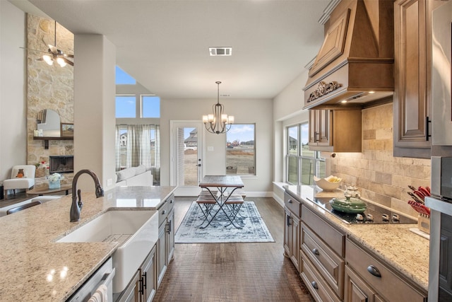 kitchen featuring sink, hanging light fixtures, custom range hood, light stone countertops, and decorative backsplash