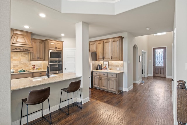 kitchen featuring sink, stainless steel appliances, light stone counters, a kitchen bar, and custom exhaust hood