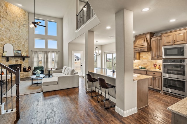 kitchen with appliances with stainless steel finishes, premium range hood, dark hardwood / wood-style floors, a fireplace, and light stone countertops