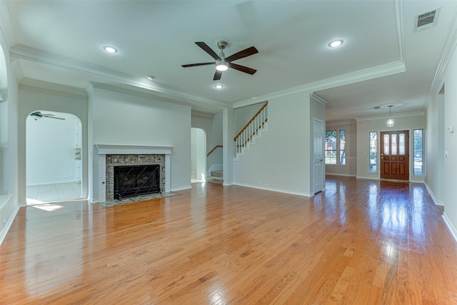 unfurnished living room with ceiling fan, ornamental molding, a tile fireplace, and light wood-type flooring