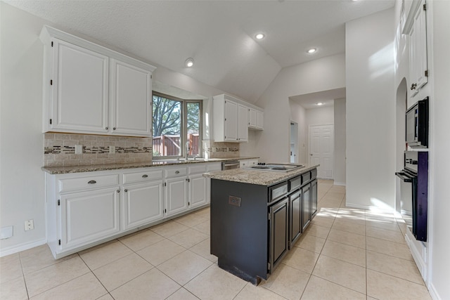 kitchen featuring light stone counters, light tile patterned floors, a kitchen island, oven, and white cabinets