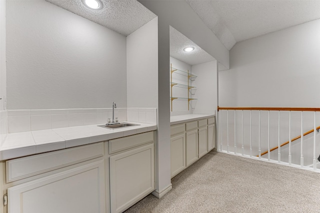 bar with light carpet, sink, tile counters, and a textured ceiling