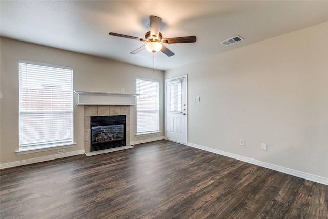 unfurnished living room with a tile fireplace, dark hardwood / wood-style floors, and ceiling fan