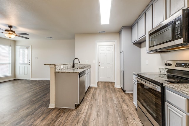 kitchen featuring appliances with stainless steel finishes, sink, gray cabinetry, light stone counters, and dark wood-type flooring