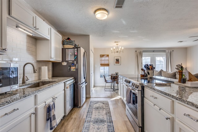 kitchen featuring appliances with stainless steel finishes, white cabinetry, sink, light stone counters, and light hardwood / wood-style floors