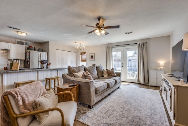 living room featuring ceiling fan with notable chandelier, a textured ceiling, light hardwood / wood-style floors, and french doors