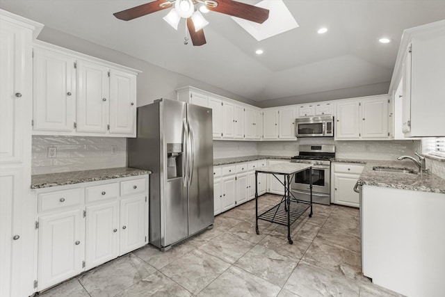 kitchen featuring sink, appliances with stainless steel finishes, lofted ceiling with skylight, light stone counters, and white cabinets