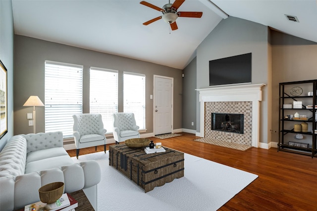 living room with dark hardwood / wood-style floors, high vaulted ceiling, beamed ceiling, a tiled fireplace, and ceiling fan