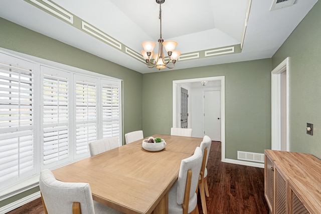 dining area with dark wood-type flooring, a tray ceiling, and an inviting chandelier