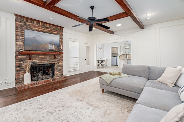 living room featuring a fireplace, washer / dryer, ceiling fan, beam ceiling, and light hardwood / wood-style flooring