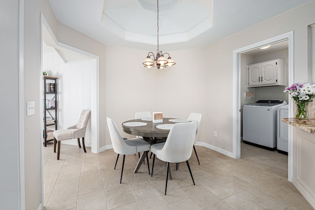 dining area with a raised ceiling, washing machine and dryer, and a notable chandelier