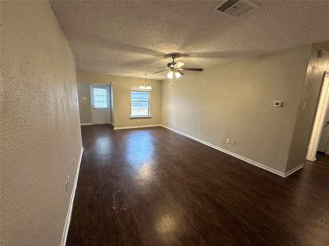 empty room featuring ceiling fan with notable chandelier, dark hardwood / wood-style floors, and a textured ceiling