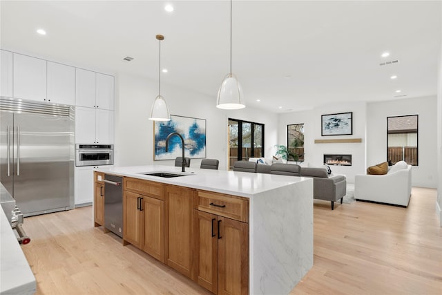 kitchen featuring sink, appliances with stainless steel finishes, white cabinetry, hanging light fixtures, and a center island with sink