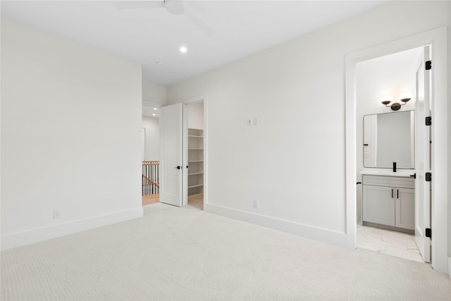 unfurnished bedroom featuring ceiling fan, a walk in closet, light carpet, and ensuite bath