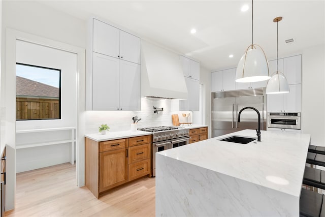 kitchen with white cabinetry, custom exhaust hood, a large island with sink, and high quality appliances