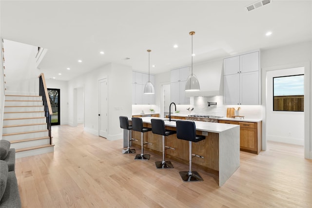 kitchen with white cabinetry, tasteful backsplash, hanging light fixtures, light wood-type flooring, and a large island