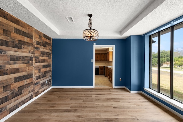 unfurnished dining area featuring an inviting chandelier, light hardwood / wood-style flooring, a raised ceiling, and wooden walls