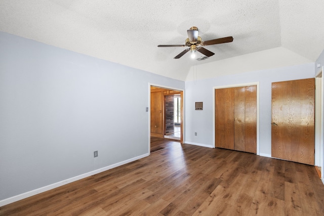 unfurnished bedroom with lofted ceiling, ceiling fan, multiple closets, dark wood-type flooring, and a textured ceiling