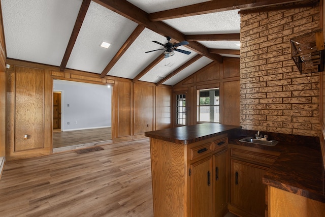 kitchen with sink, vaulted ceiling with beams, a textured ceiling, light hardwood / wood-style flooring, and kitchen peninsula