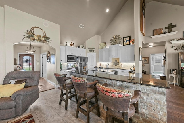 kitchen featuring dark stone countertops, a kitchen breakfast bar, stainless steel appliances, white cabinets, and kitchen peninsula