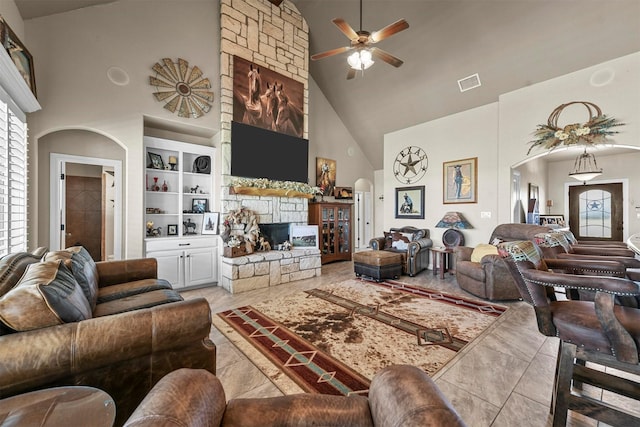 living room with ceiling fan, a fireplace, built in features, and a high ceiling