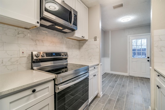 kitchen featuring appliances with stainless steel finishes, white cabinets, a textured ceiling, and decorative backsplash