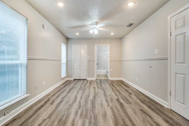 unfurnished bedroom with ensuite bath, light hardwood / wood-style flooring, a textured ceiling, a closet, and ceiling fan