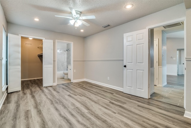 unfurnished bedroom featuring connected bathroom, a spacious closet, light hardwood / wood-style flooring, a textured ceiling, and a closet