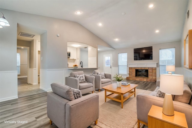 living room featuring vaulted ceiling, a stone fireplace, and light hardwood / wood-style flooring