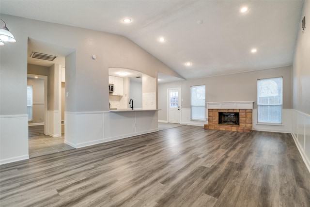 unfurnished living room featuring lofted ceiling, hardwood / wood-style floors, and a stone fireplace