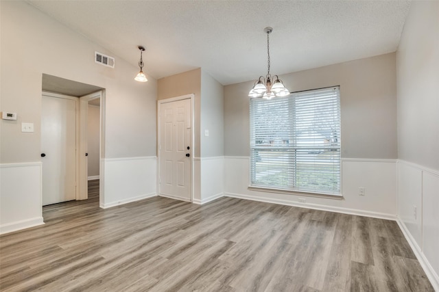 spare room with vaulted ceiling, a textured ceiling, a notable chandelier, and light hardwood / wood-style floors